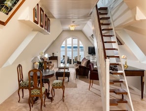 Un loft espacioso con techo alto, un comedor con una mesa y sillas redondas, una zona de estar acogedora con sofás, una escalera y un amplio ventanal de arco que ofrece vistas.