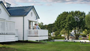 A white house with a blue roof, a balcony, and a well-maintained lawn with outdoor furniture.