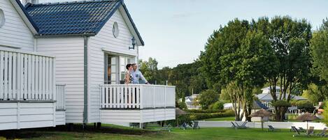 A white house with a blue roof, a balcony, and a well-maintained lawn with outdoor furniture.