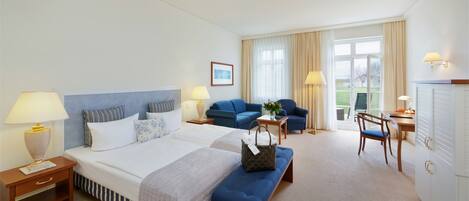 A hotel room with a large bed, two bedside tables, a desk, a chair, a sofa, and a view of the outdoors.