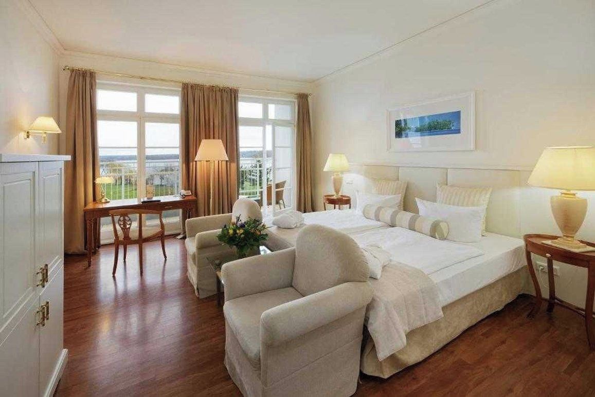 A hotel room with a bed, two bedside tables, a desk, a chair, and a view of the outdoors.