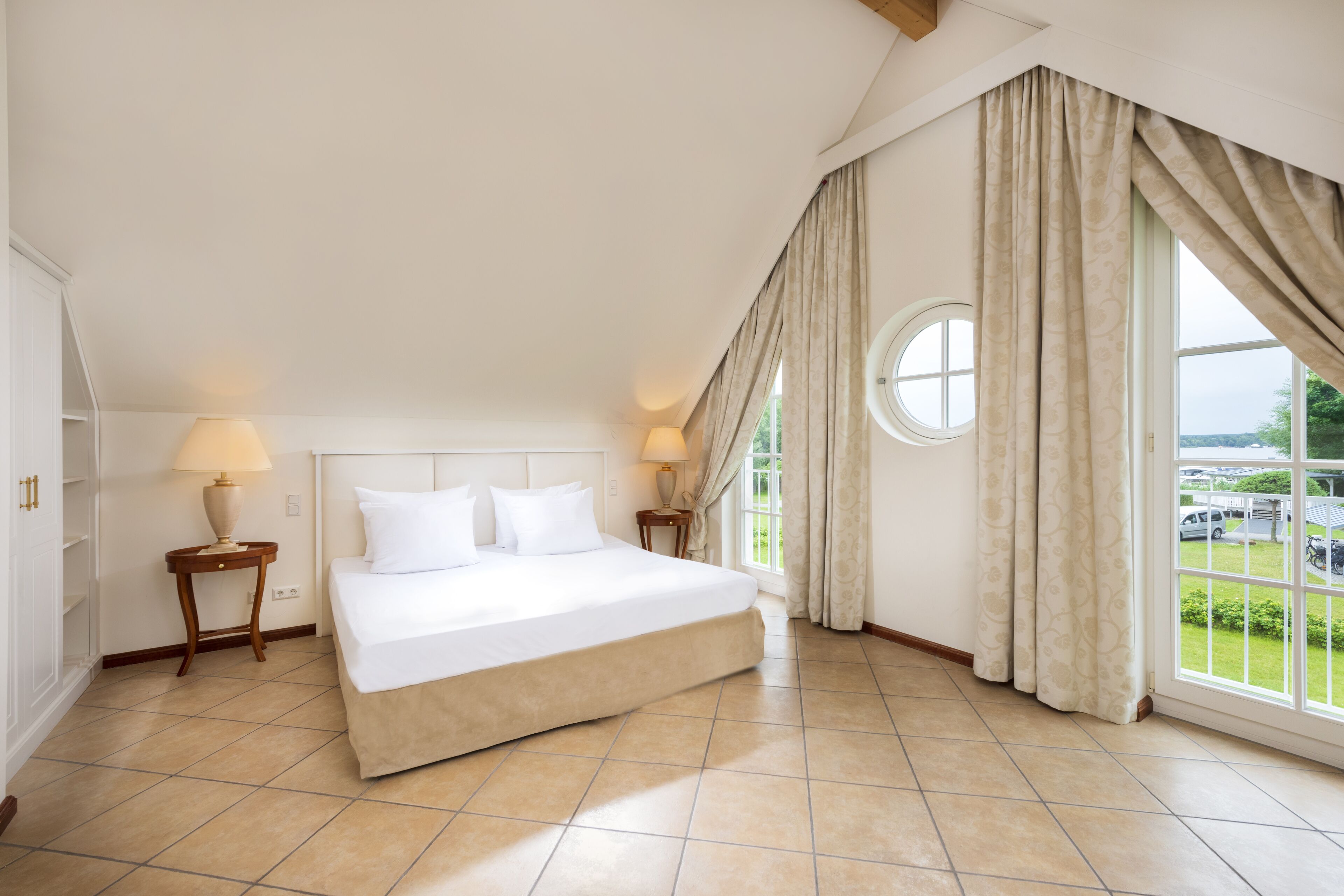Une chambre spacieuse avec un grand lit, deux tables de chevet avec des lampes, une fenêtre avec des rideaux et une vue sur l  ’extérieur.
