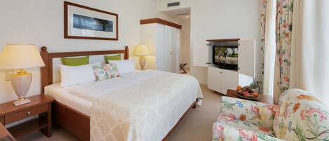 Una habitación de hotel con cama, dos lámparas de noche, televisor, sillón floral y armario.