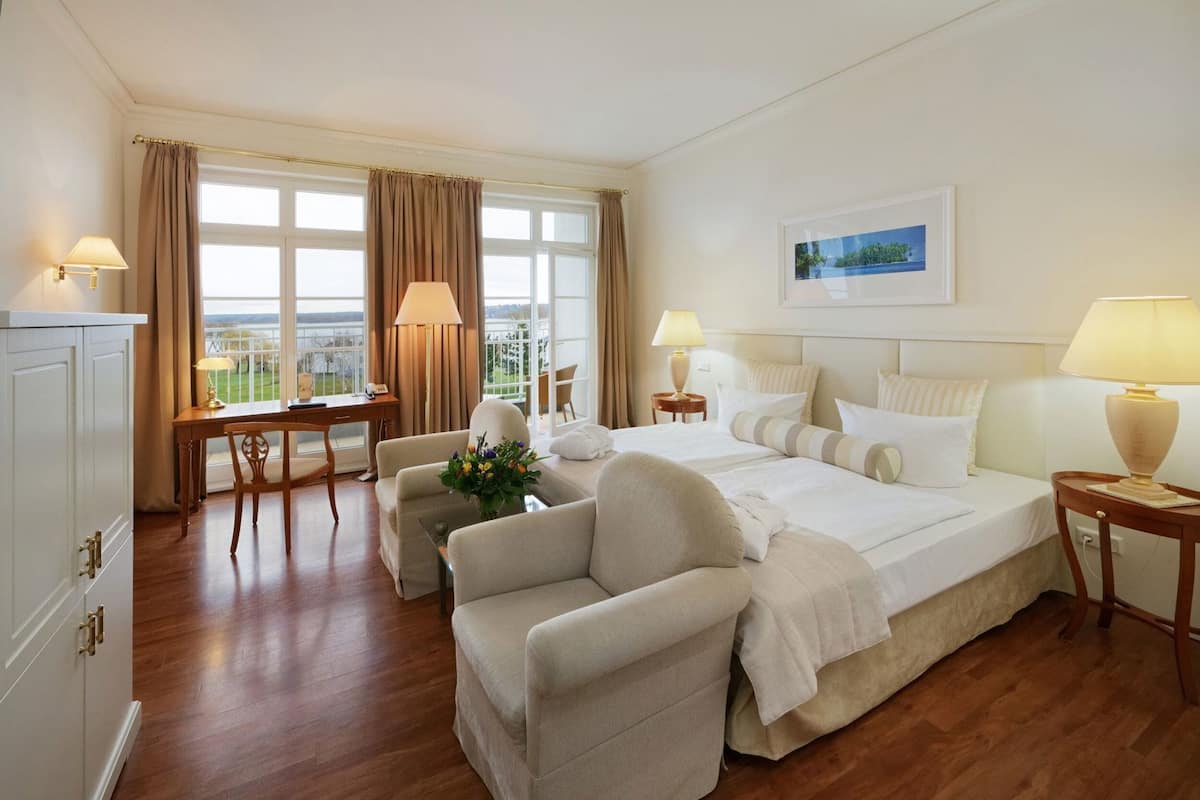 A hotel room with a bed, two chairs, a desk, and a view of the outdoors.