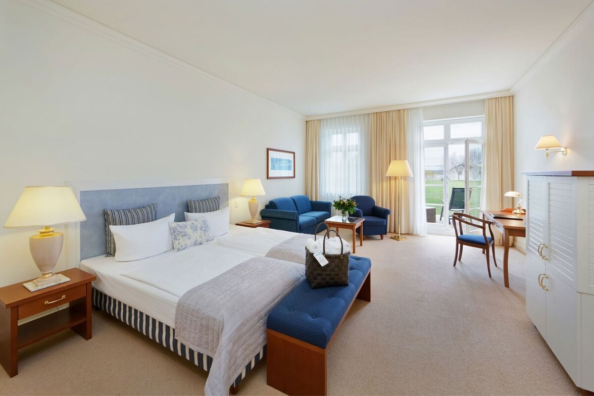 A hotel room with a bed, bedside tables, a desk, a chair, a sofa, and a wardrobe.