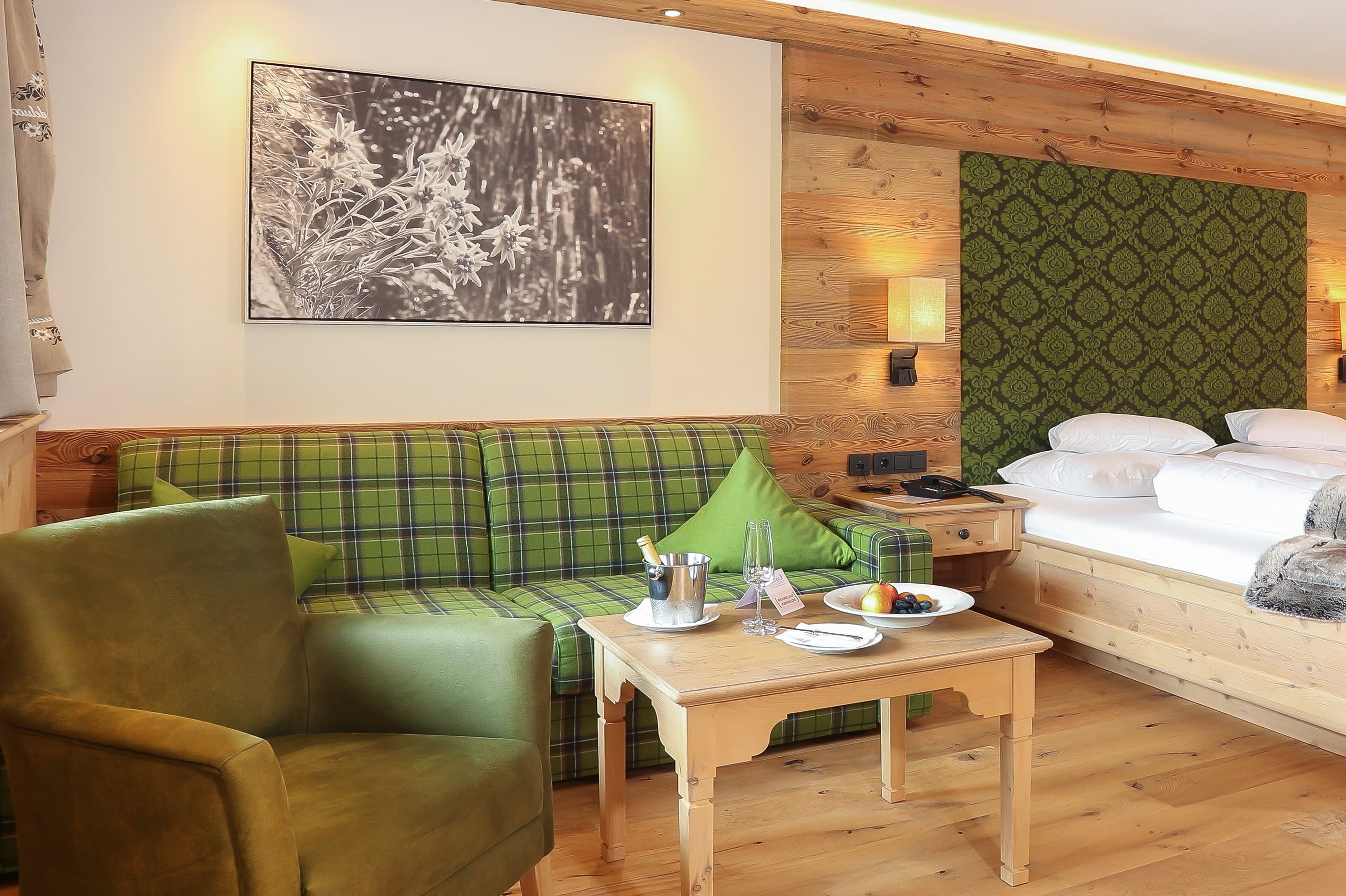 A cozy room with a plaid sofa, a wooden table with breakfast items, a bed with white linens, and a wall-mounted artwork.