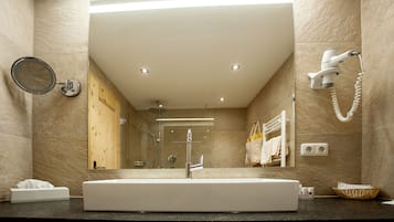 Un baño moderno con un espejo grande, un lavamanos, un cabezal de ducha de mano y un perchero para toallas.