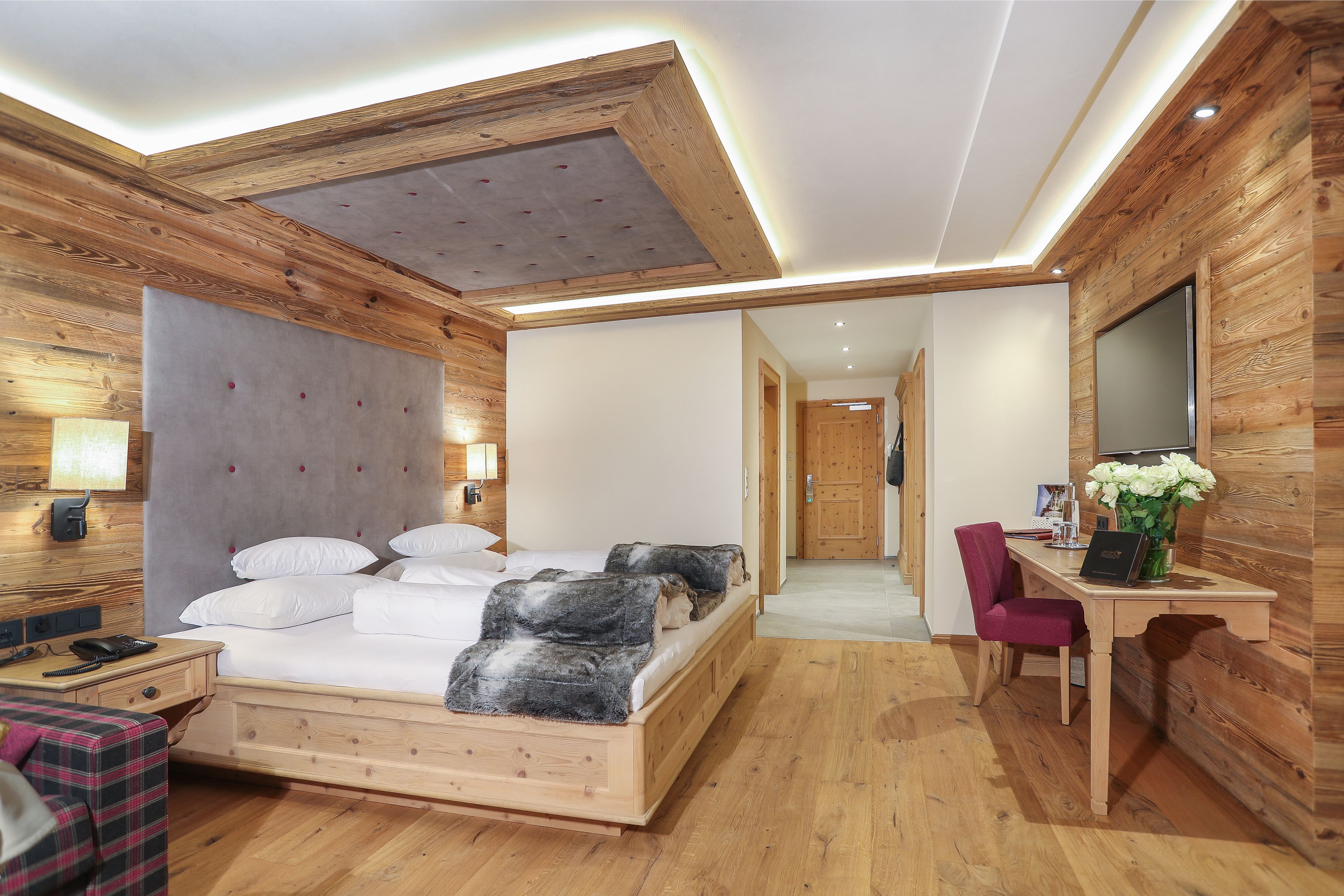 A modern bedroom with a wooden ceiling, a large bed, a desk with a chair, and a mirror.