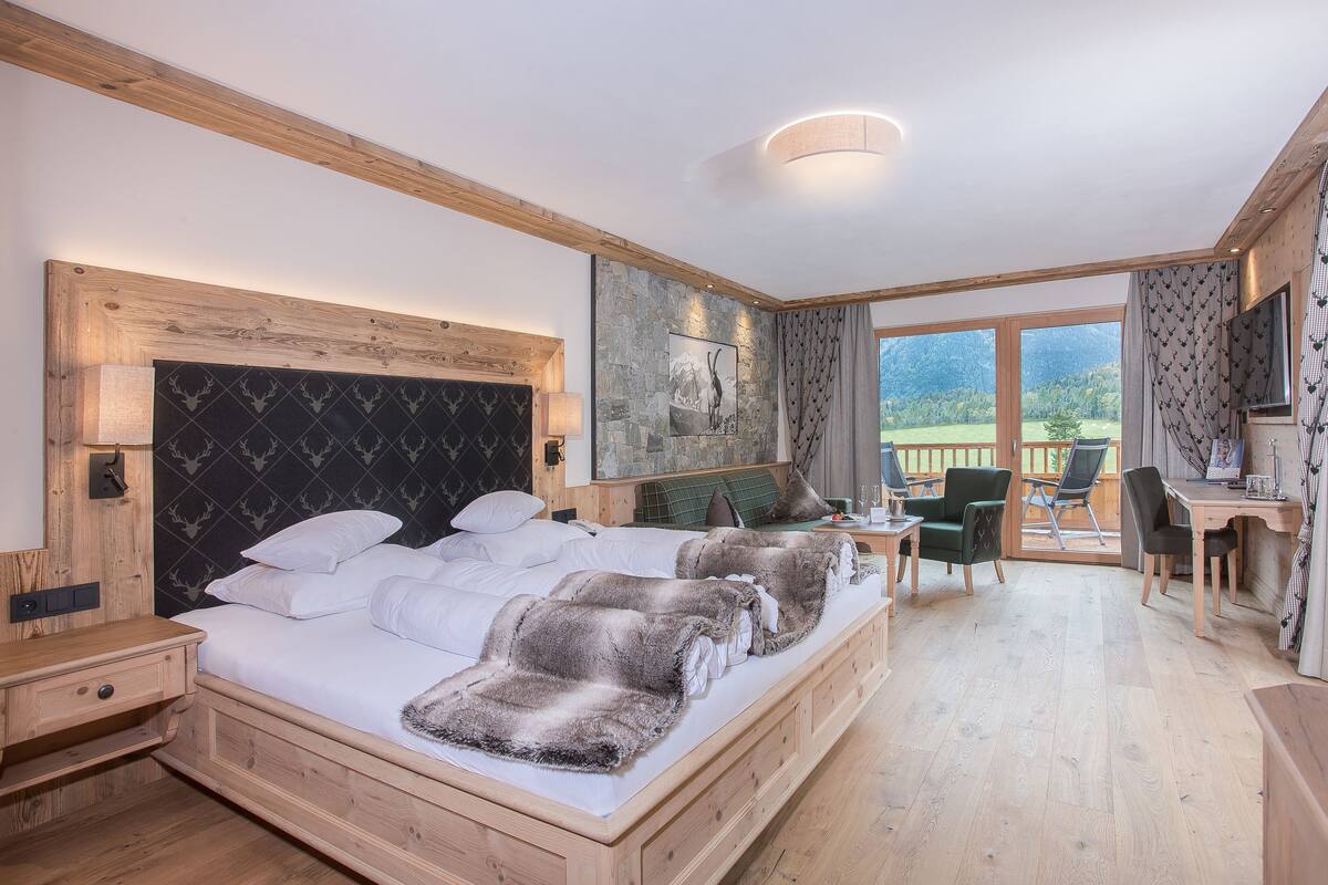 A bedroom with a wooden bed, a desk, and a view of the outdoors.