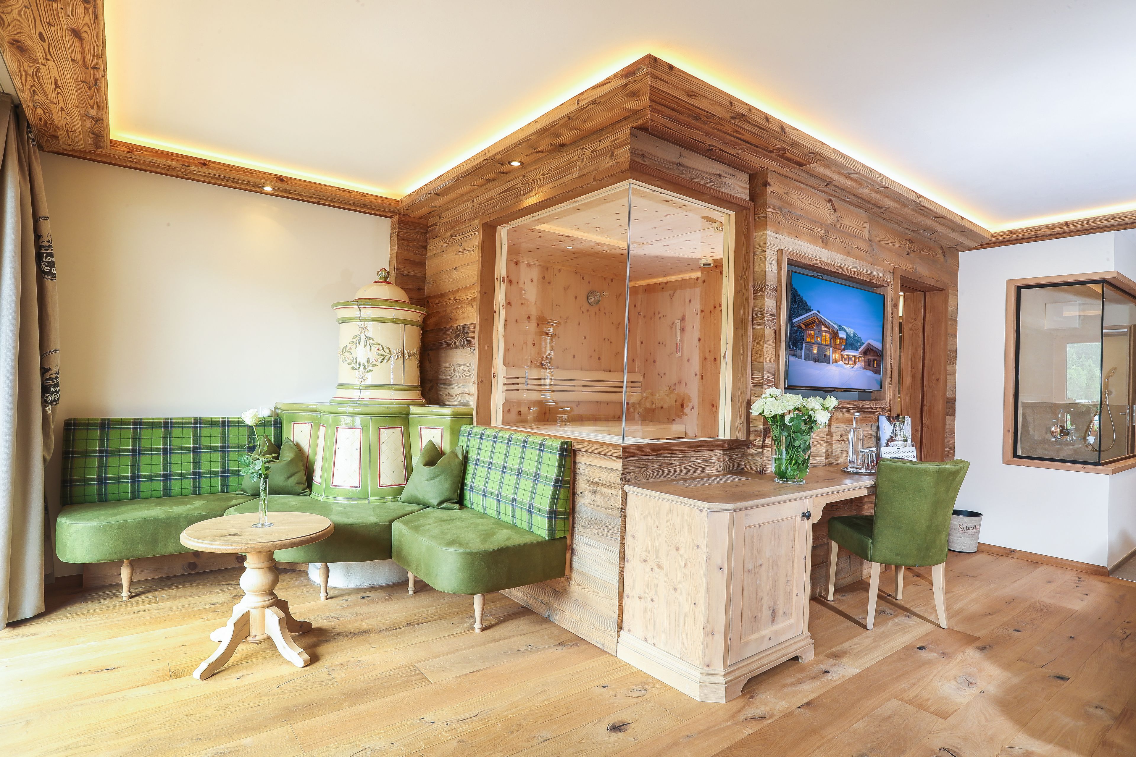 A cozy living room with a green sofa, a wooden cabinet, and a television mounted on the wall.