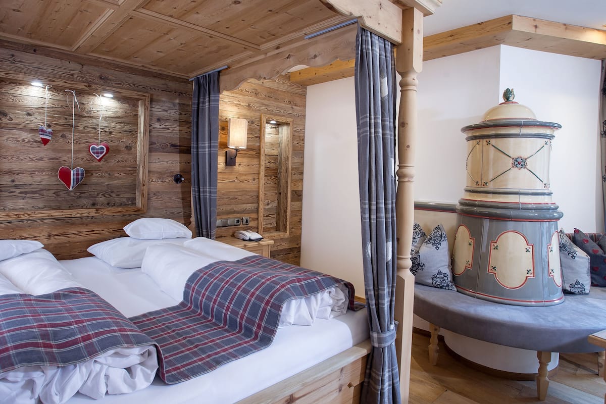 A wooden cabin-style room with a bed, a wooden headboard, a mirror, a lamp, and a decorative wooden column.