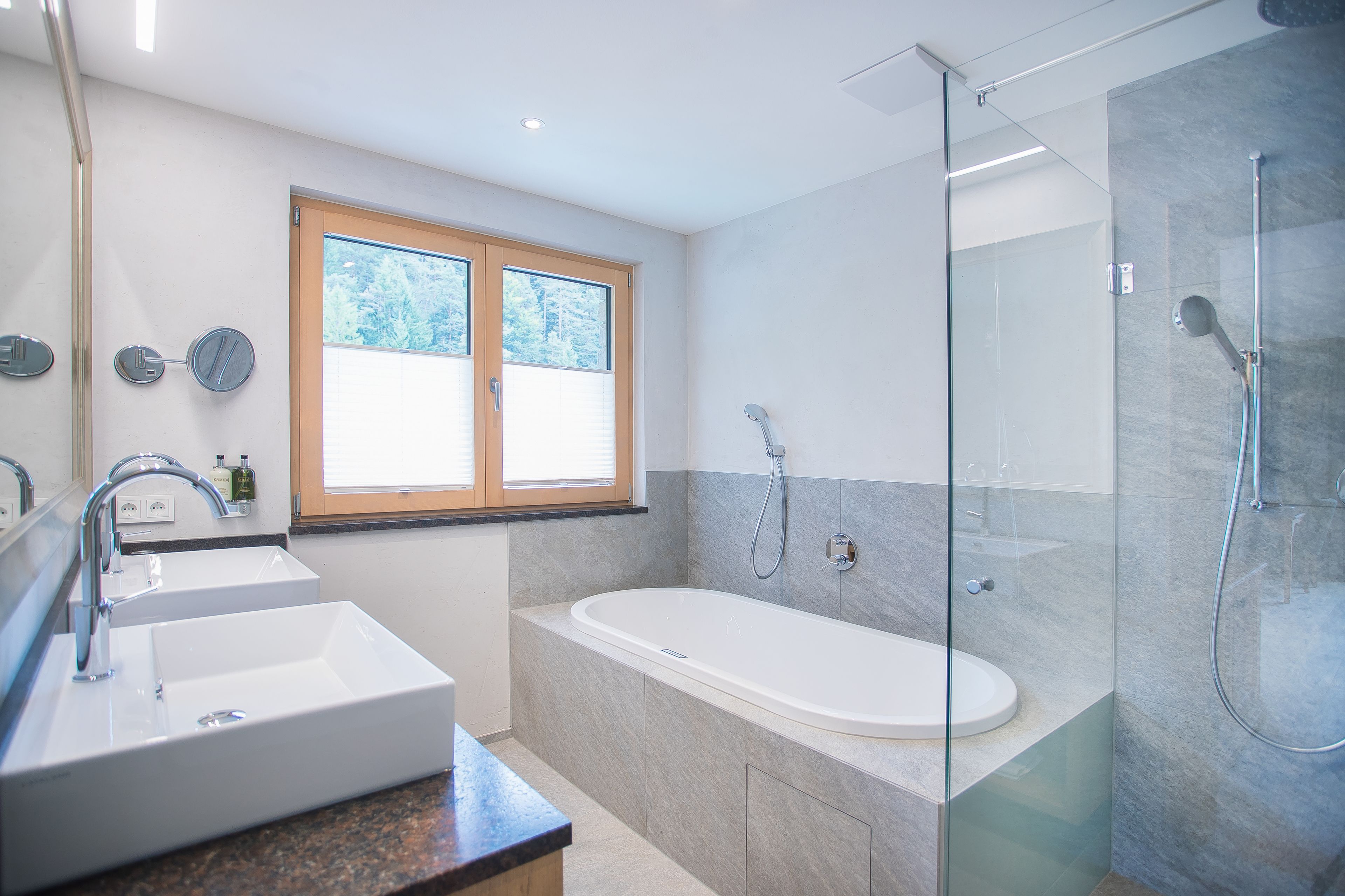 A modern bathroom with a double sink, a glass-enclosed shower, and a large window.