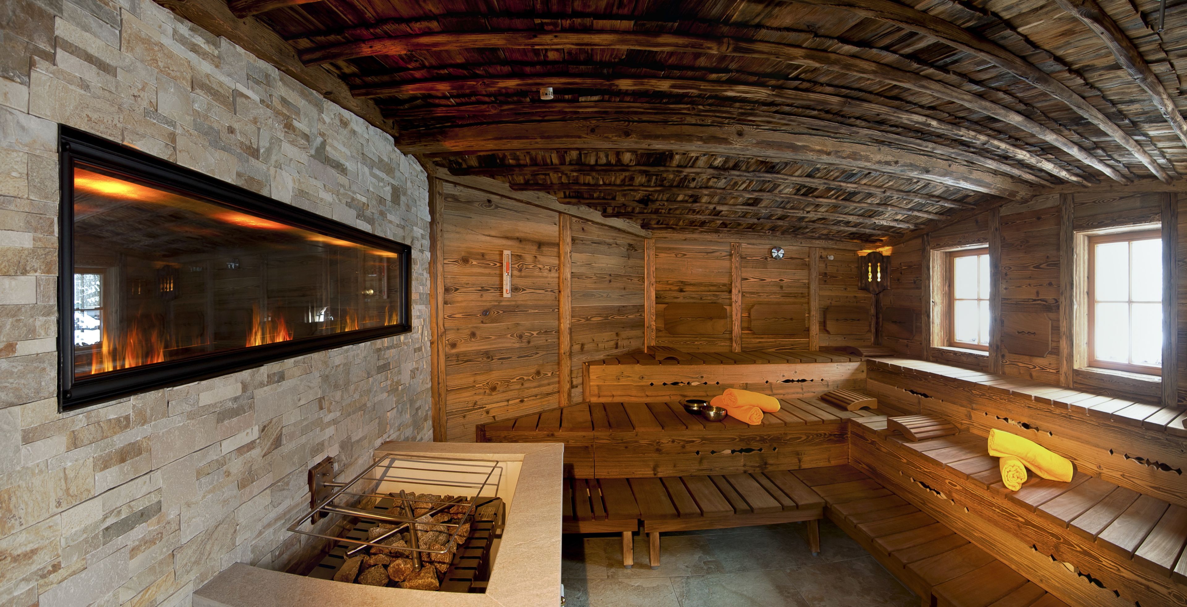 Una sauna con paredes de piedra, bancos de madera y una chimenea empotrada con cristales.