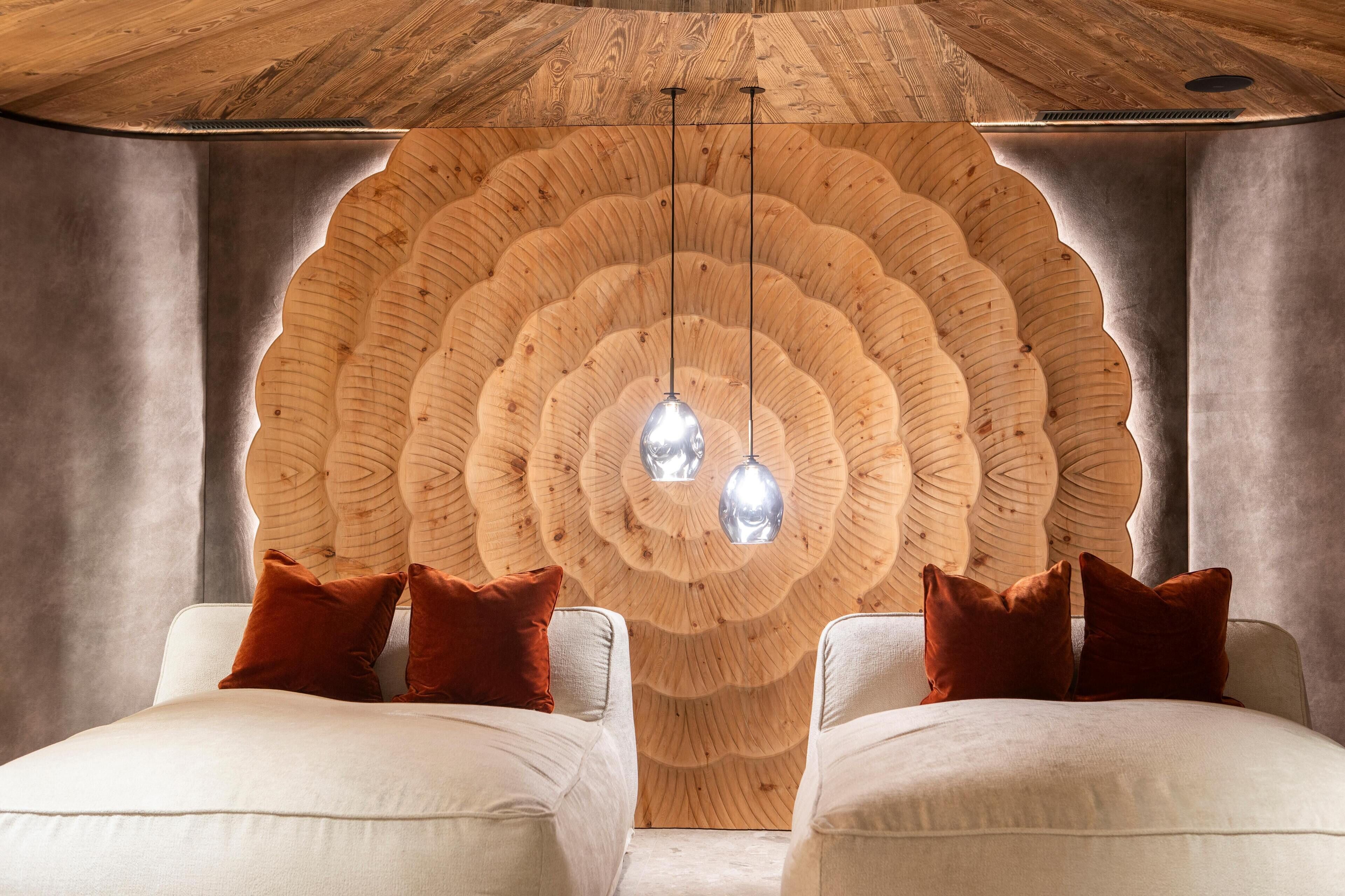Una habitación con un diseño único en la pared de madera, dos sofás blancos con cojines marrones e iluminación colgante.