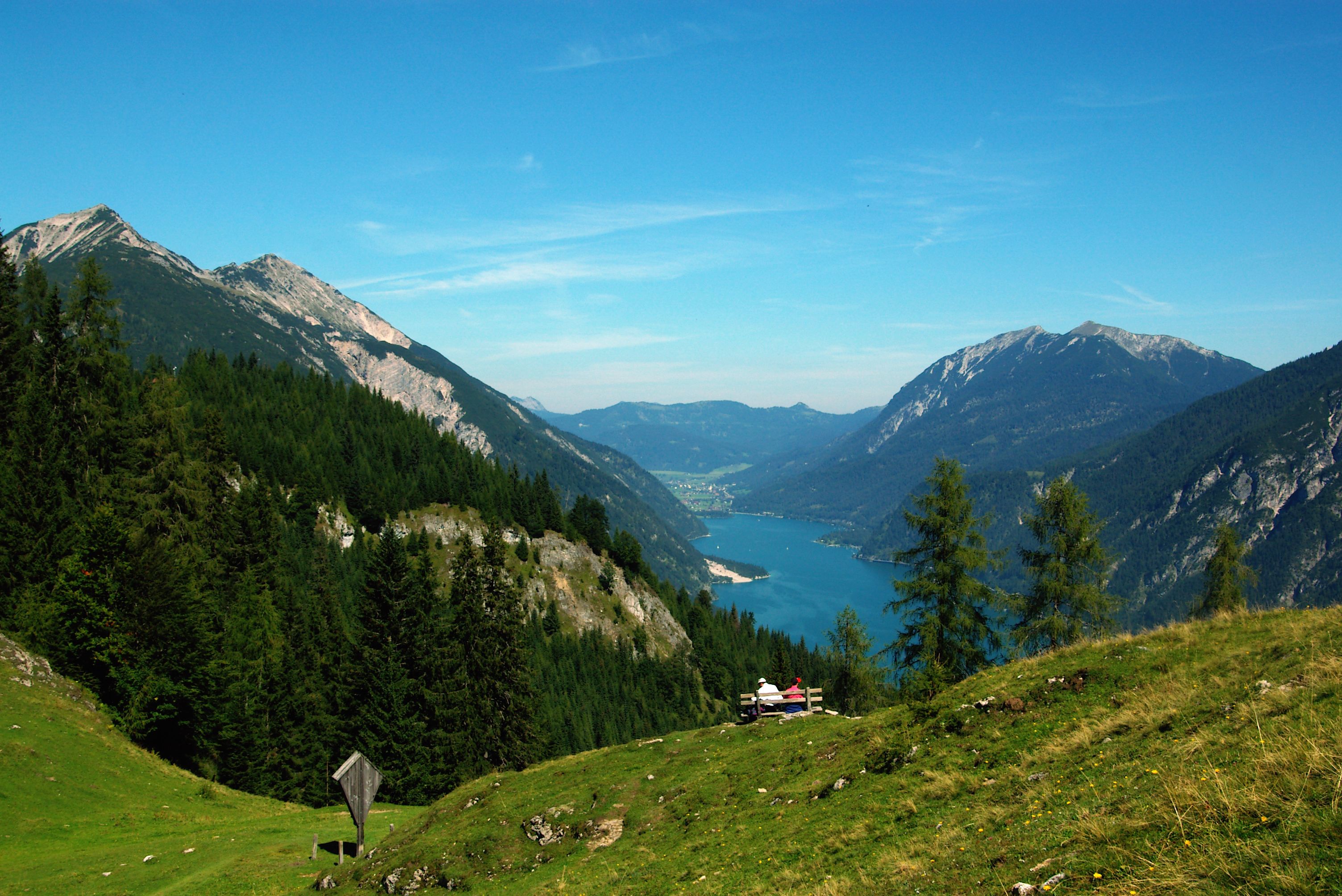 A scenic mountain landscape with a lake and a bench overlooking the view.