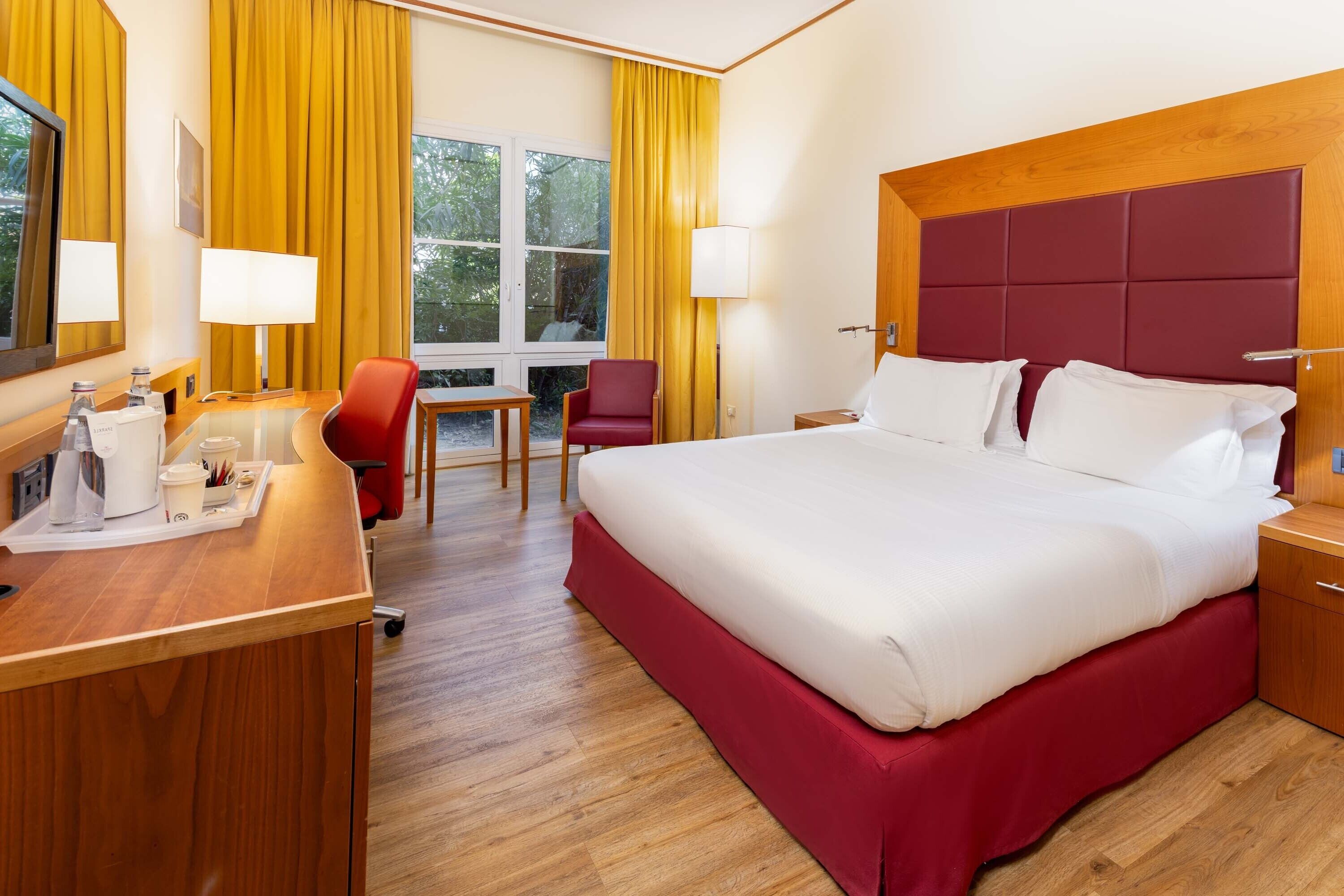 Een hotelkamer met een groot bed, een bureau met stoel, een bijzettafeltje en twee lampen.