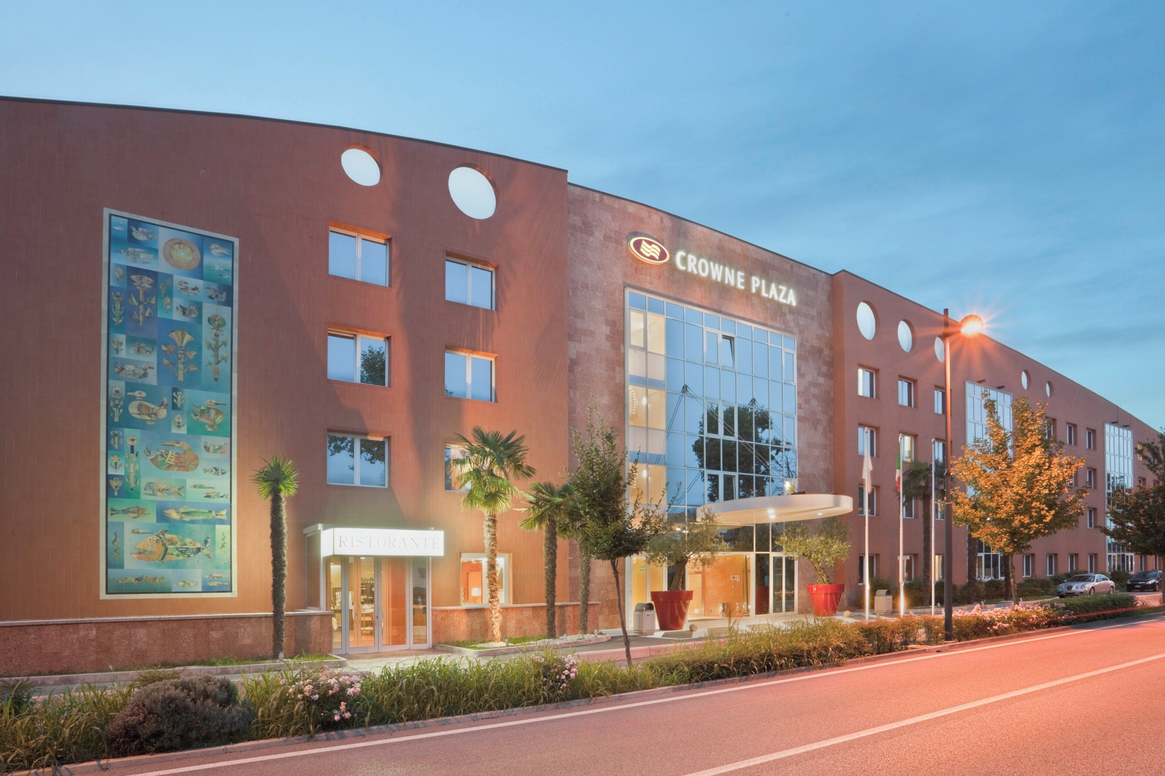 A modern building with a large glass facade, a sign reading 'CROWNE PLAZA,' and a restaurant entrance.