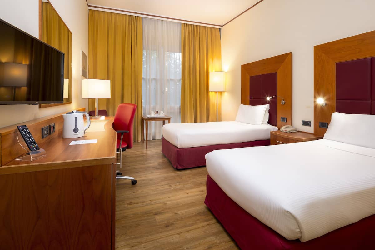 Ein Hotelzimmer mit zwei Betten, einem Schreibtisch, einem Telefon, einem Fernseher und einem Sessel.
