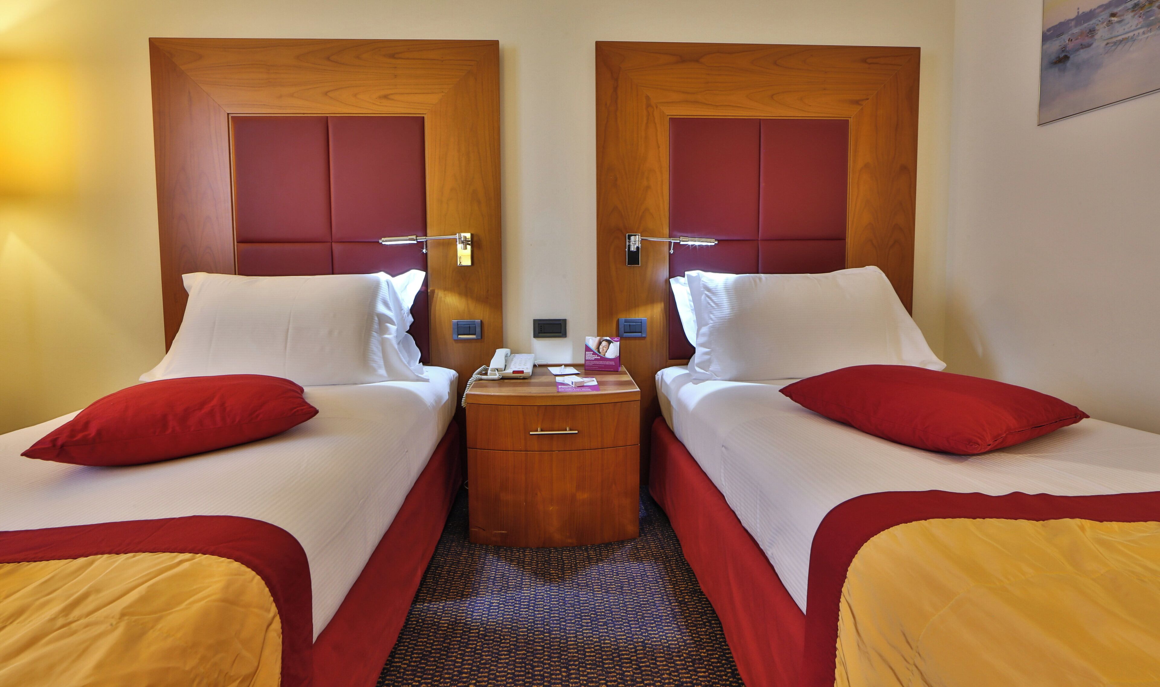 A hotel room with two beds, a wooden nightstand, a telephone, and a small table.