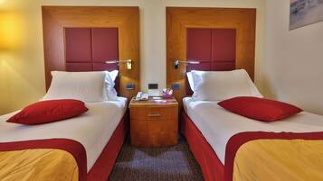 A hotel room with two beds, a wooden nightstand, a telephone, and a small table.