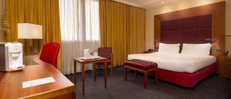 A hotel room with a bed, a desk, a chair, a table, and a lamp.