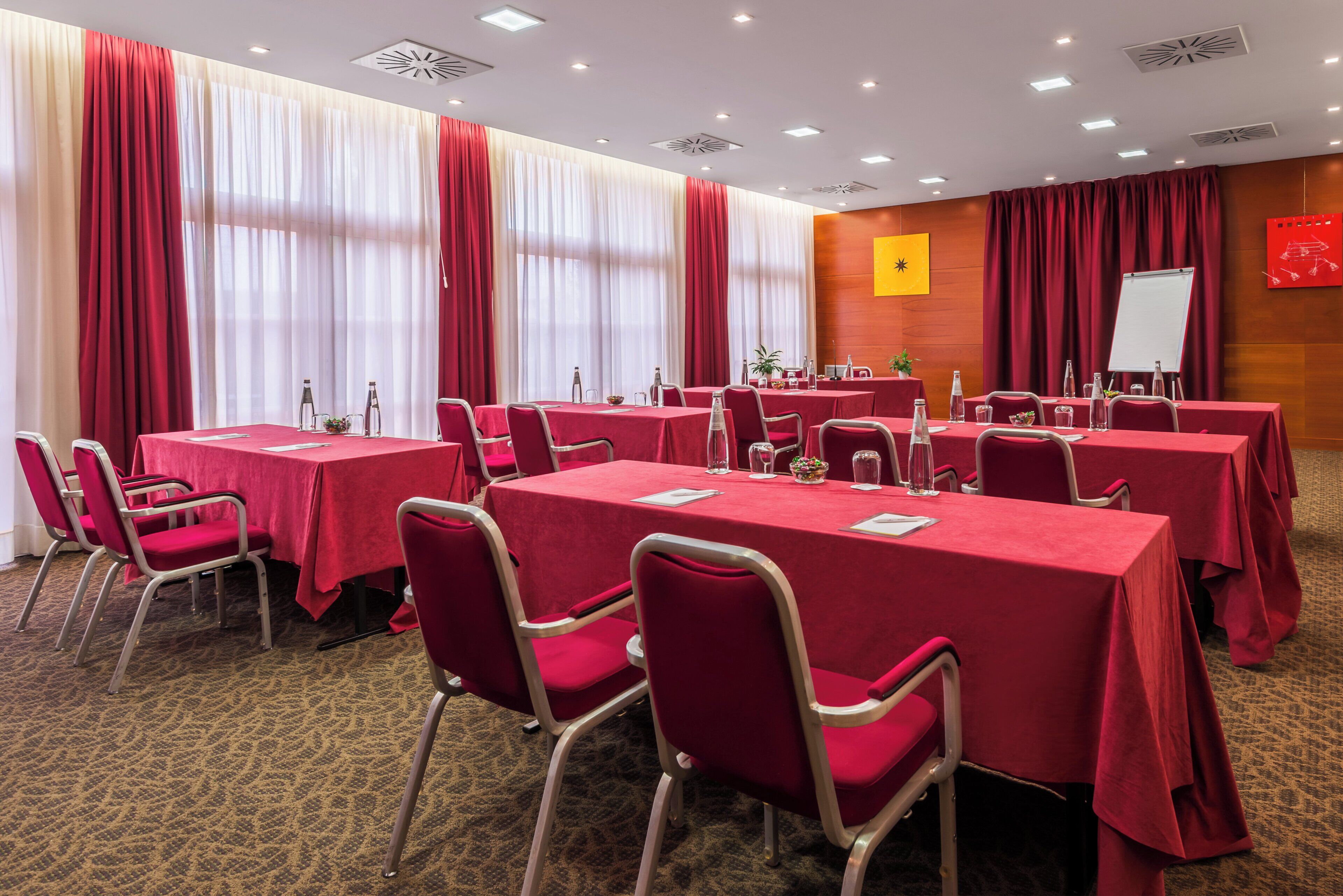 A conference room with multiple tables and chairs, a whiteboard, and a red curtain.