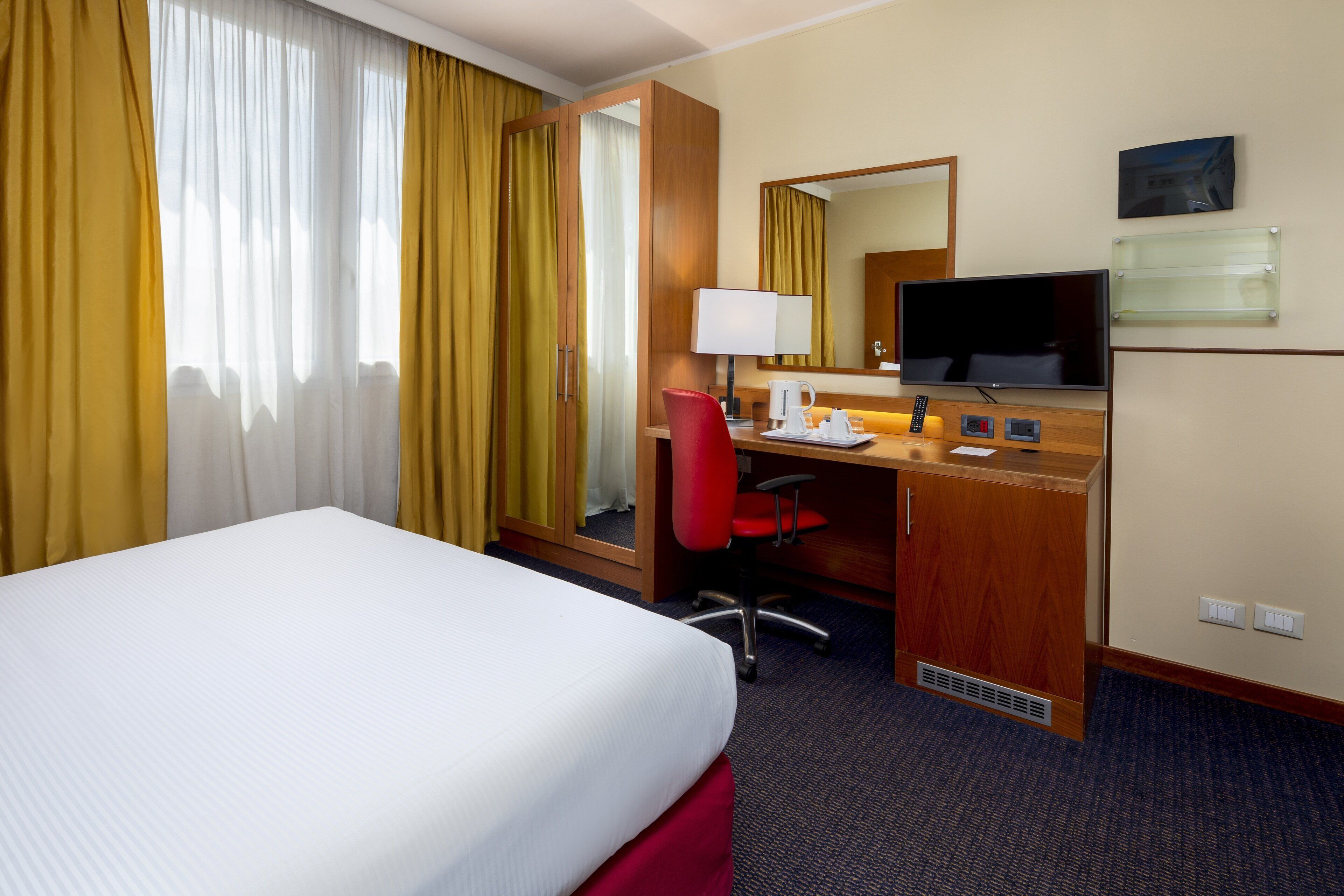 A hotel room with a bed, desk, chair, TV, and a mirror.