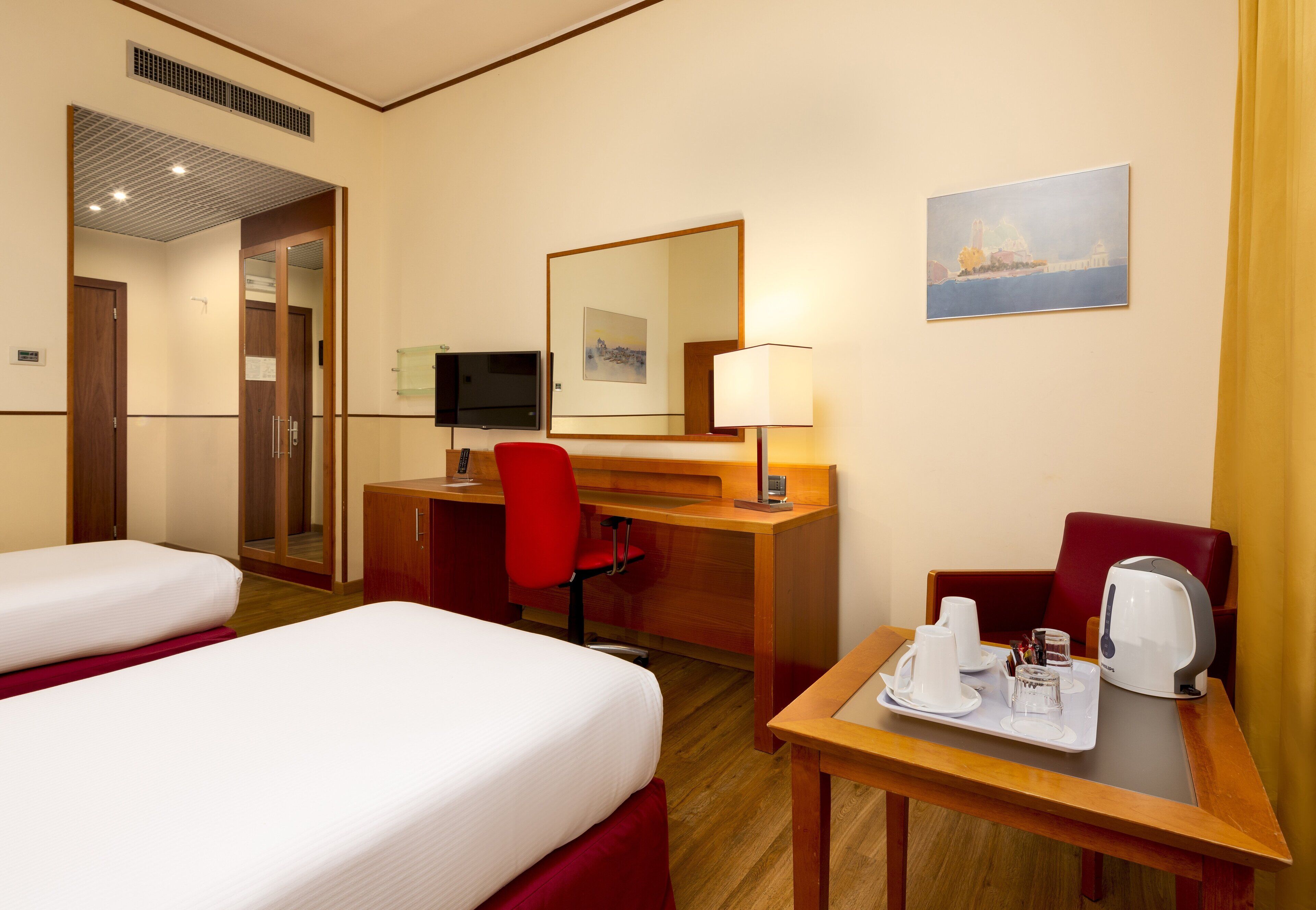 Habitación de hotel con dos camas, un escritorio con una silla, un televisor, un cuadro y una mesa con una bandeja de alimentos para el desayuno.