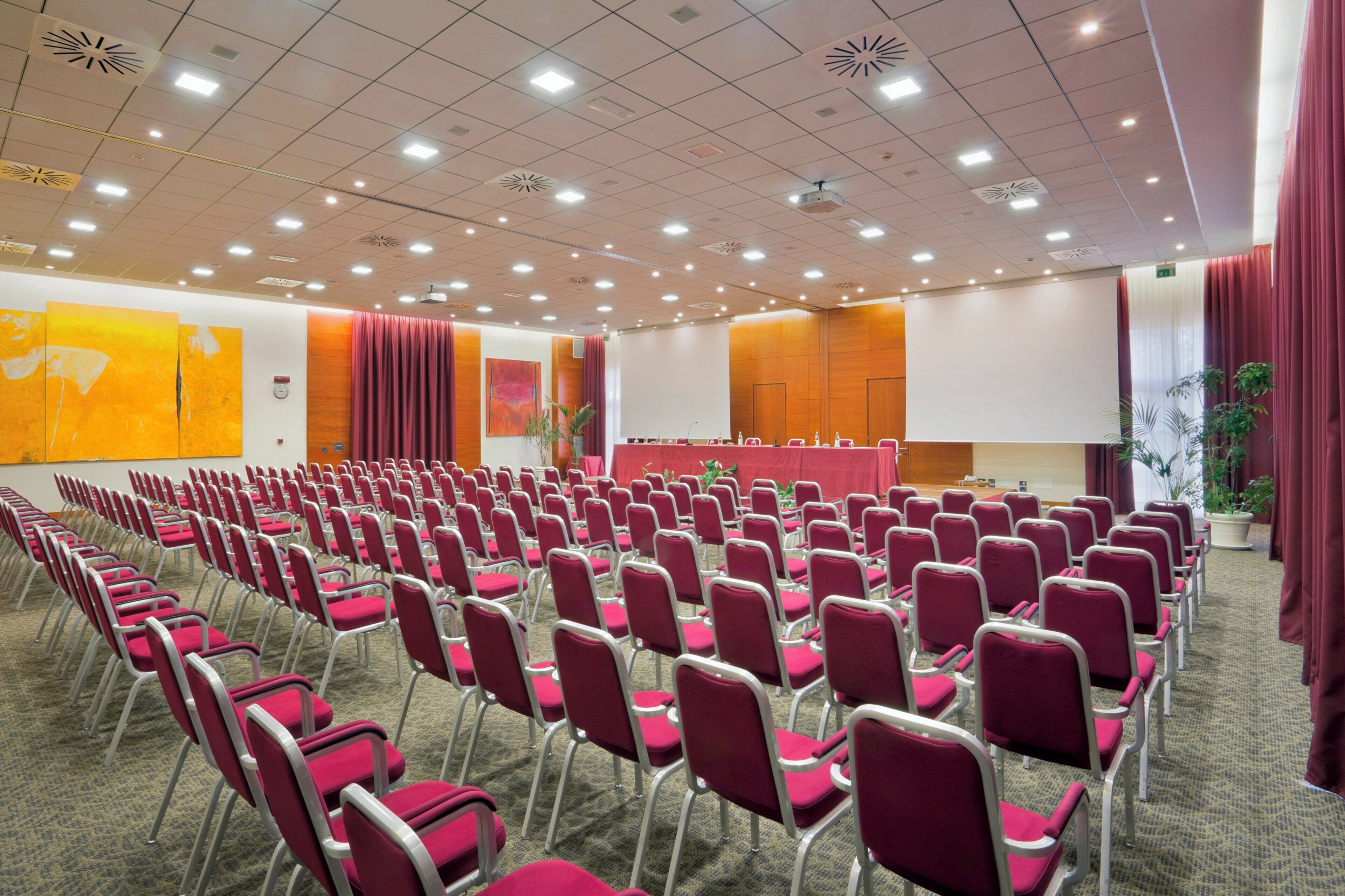 A conference room with rows of chairs, a stage, and a projector.