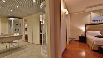 A hotel room with a bed, a bedside table, a chair, a bathroom with a shower, and a large mirror.
