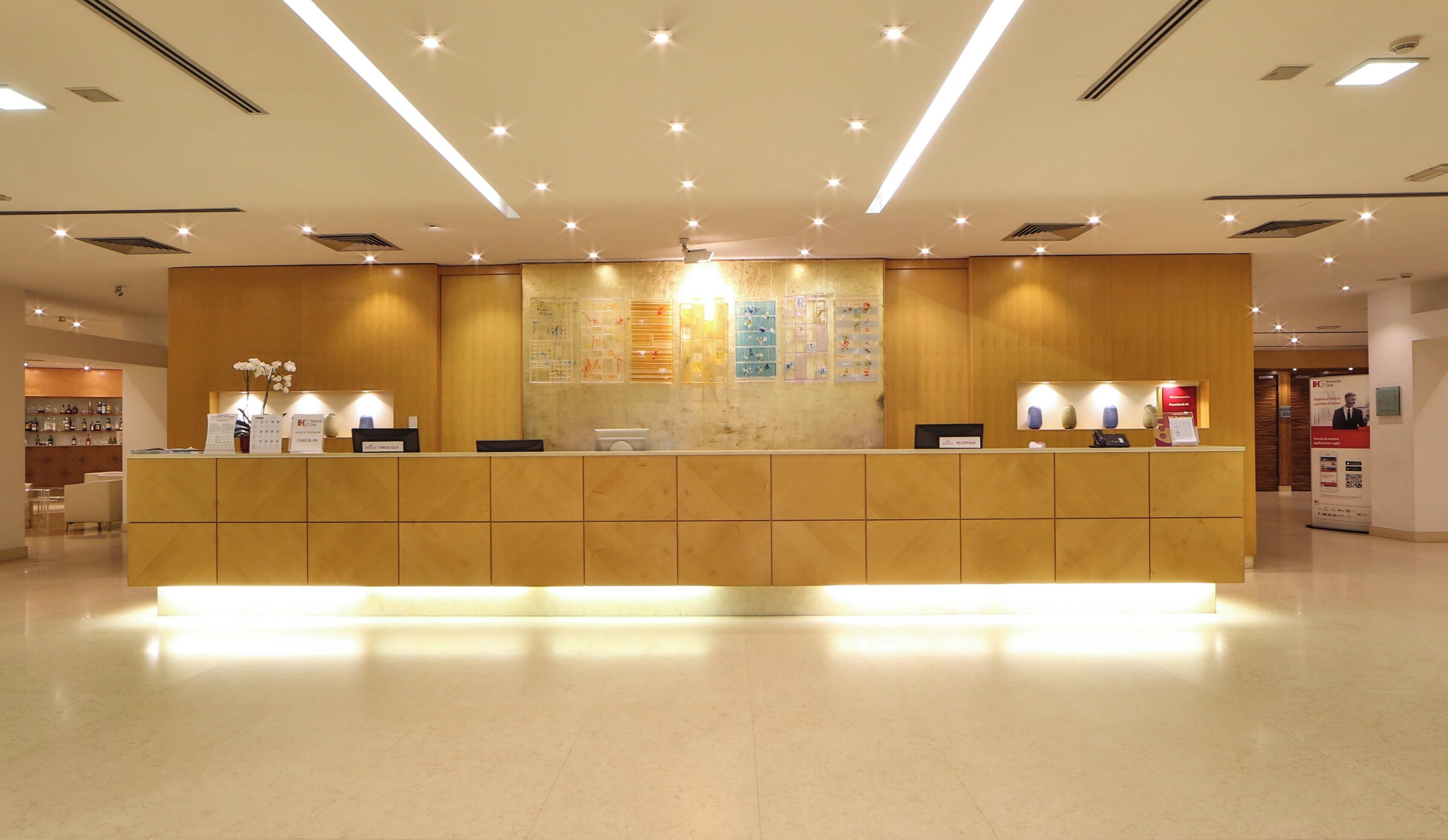 Un mostrador de recepción de hotel con detalles de madera, un tablón de anuncios y un área de recepción con piso de baldosas limpias.