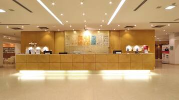 Un mostrador de recepción de hotel con detalles de madera, un tablón de anuncios y un área de recepción con piso de baldosas limpias.