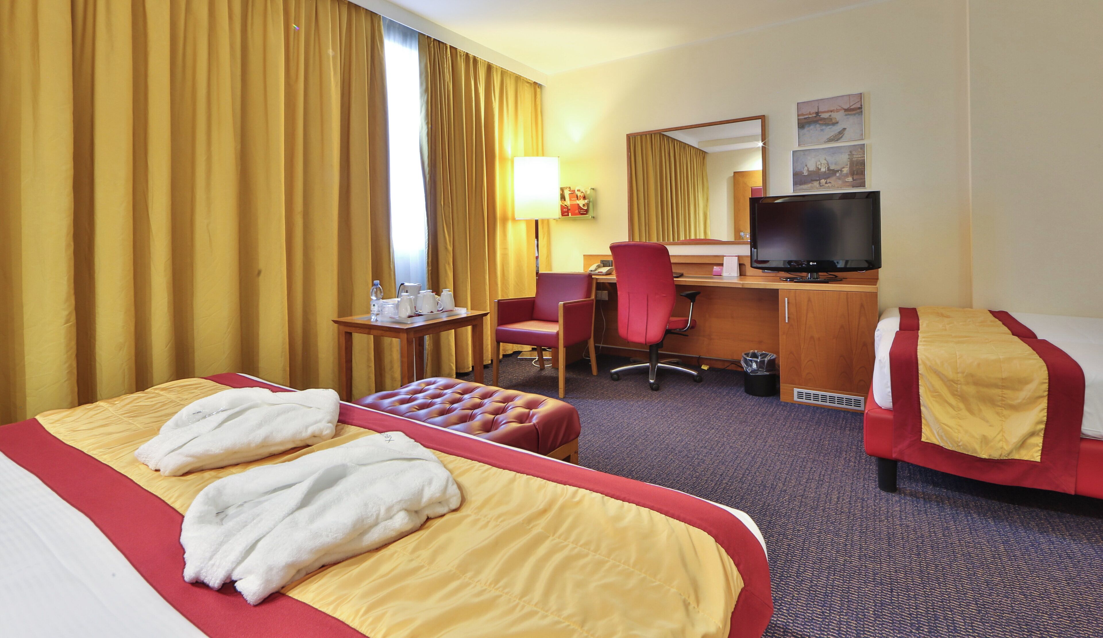 A hotel room with a bed, a desk, a chair, a television, and a window with curtains.