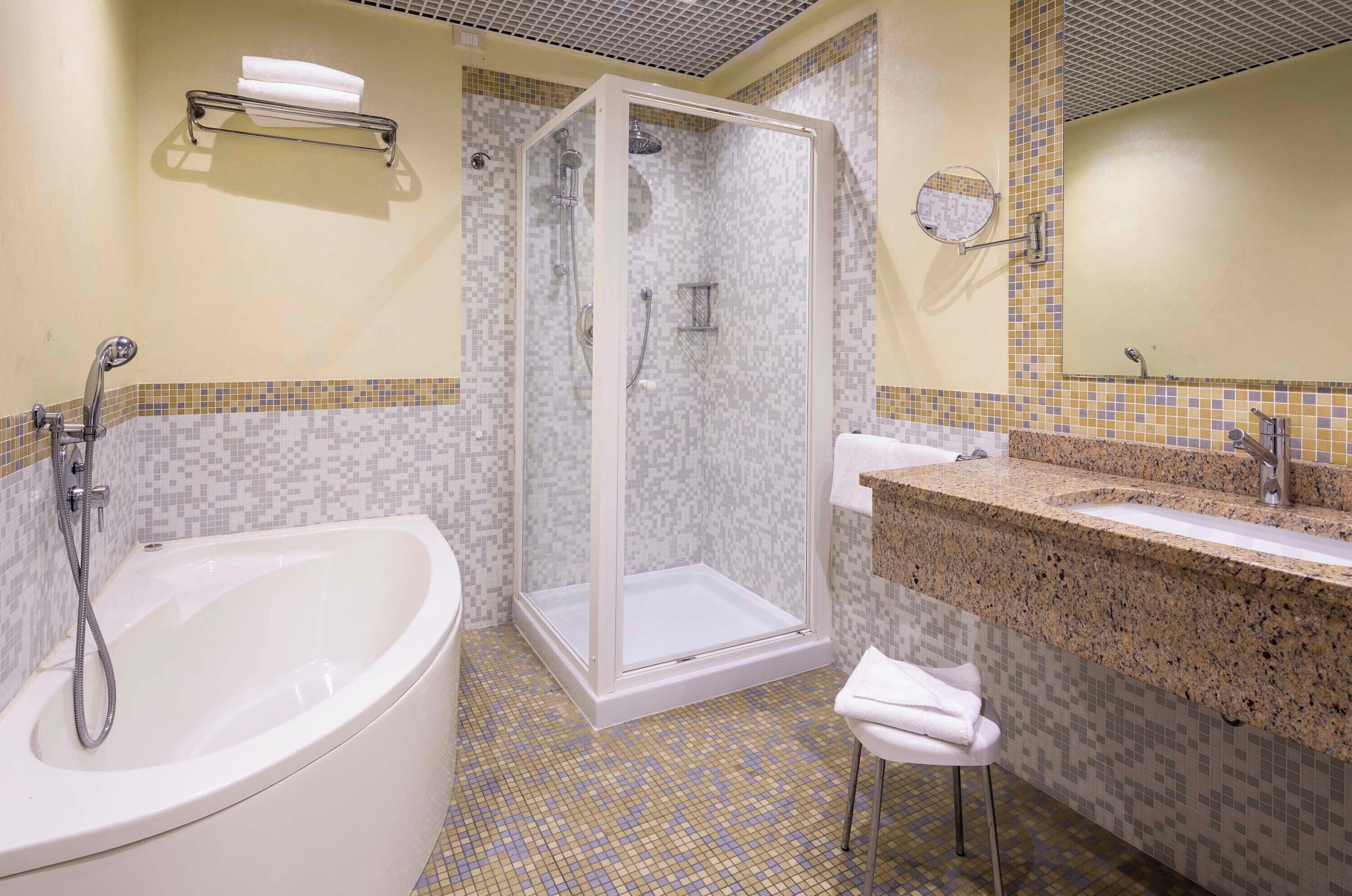 A bathroom with a bathtub, a shower enclosure, and a sink with a granite countertop.