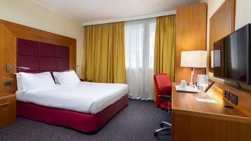 Una habitación de hotel con una cama grande, un escritorio con lámpara, una silla y un televisor.