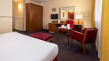 Una habitación de hotel con cama, escritorio, silla, televisor y armario.