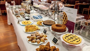 Una mesa de buffet con diversos alimentos, incluyendo pasteles y postres, en un entorno de hotel.