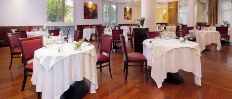 Un restaurante con mesas redondas, sillas rojas y manteles blancos.