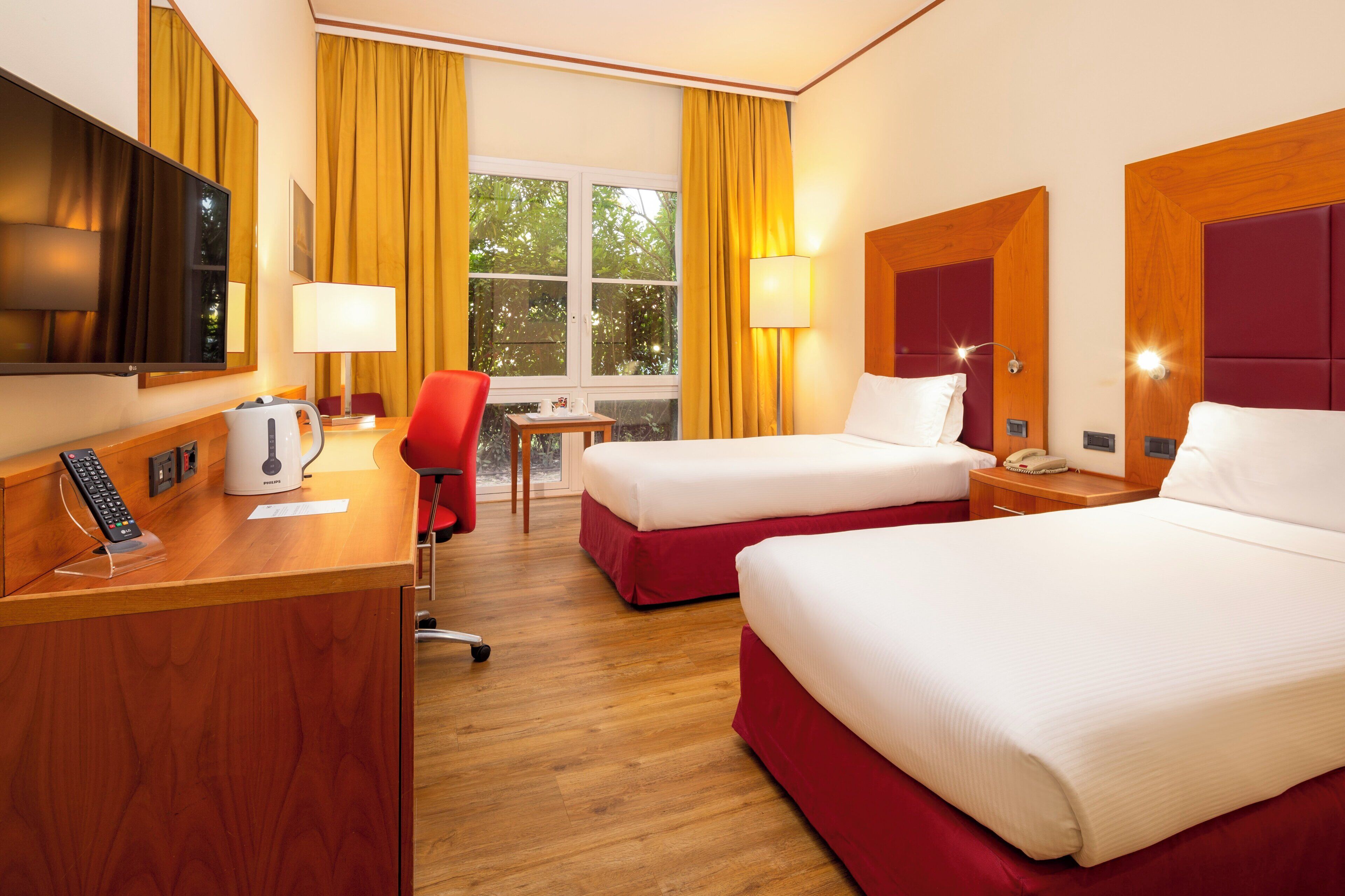 Habitación de hotel con dos camas, un escritorio con lámpara, una silla y una televisión.