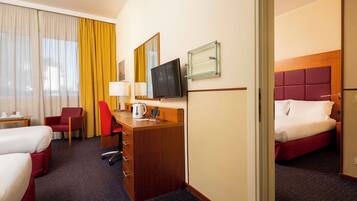 A hotel room with two beds, a desk with a chair, a television, and a window with curtains.