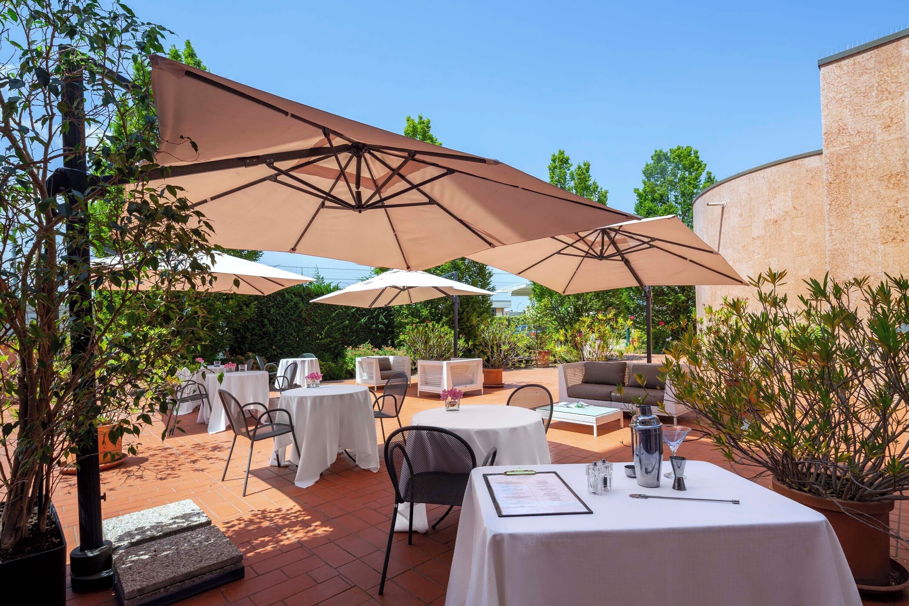 Een terras buiten met ronde tafels, stoelen en grote parasols voor de schaduw.