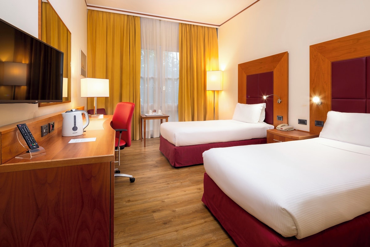 Une chambre d’hôtel avec deux lits, un bureau avec un téléphone, une télévision et une chaise.