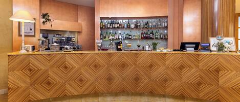 A bar area with a wooden patterned counter, shelves of liquor bottles, a coffee machine, and a cash register.