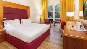 Een hotelkamer met een groot bed, een bureau met stoel, een koffiezetapparaat en een raam met gordijnen.