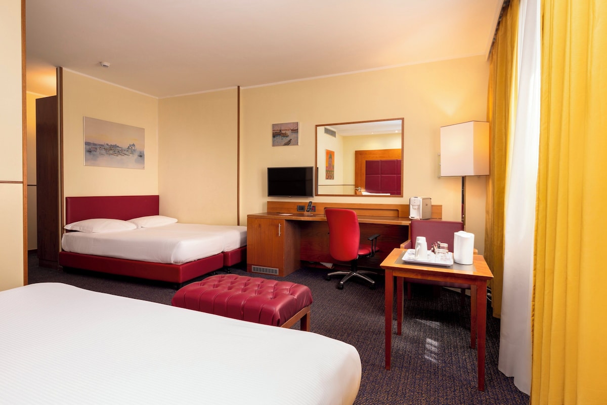 Une chambre d’hôtel équipée d’un lit, d’un bureau, d’une chaise, d’une télévision et d’un miroir.