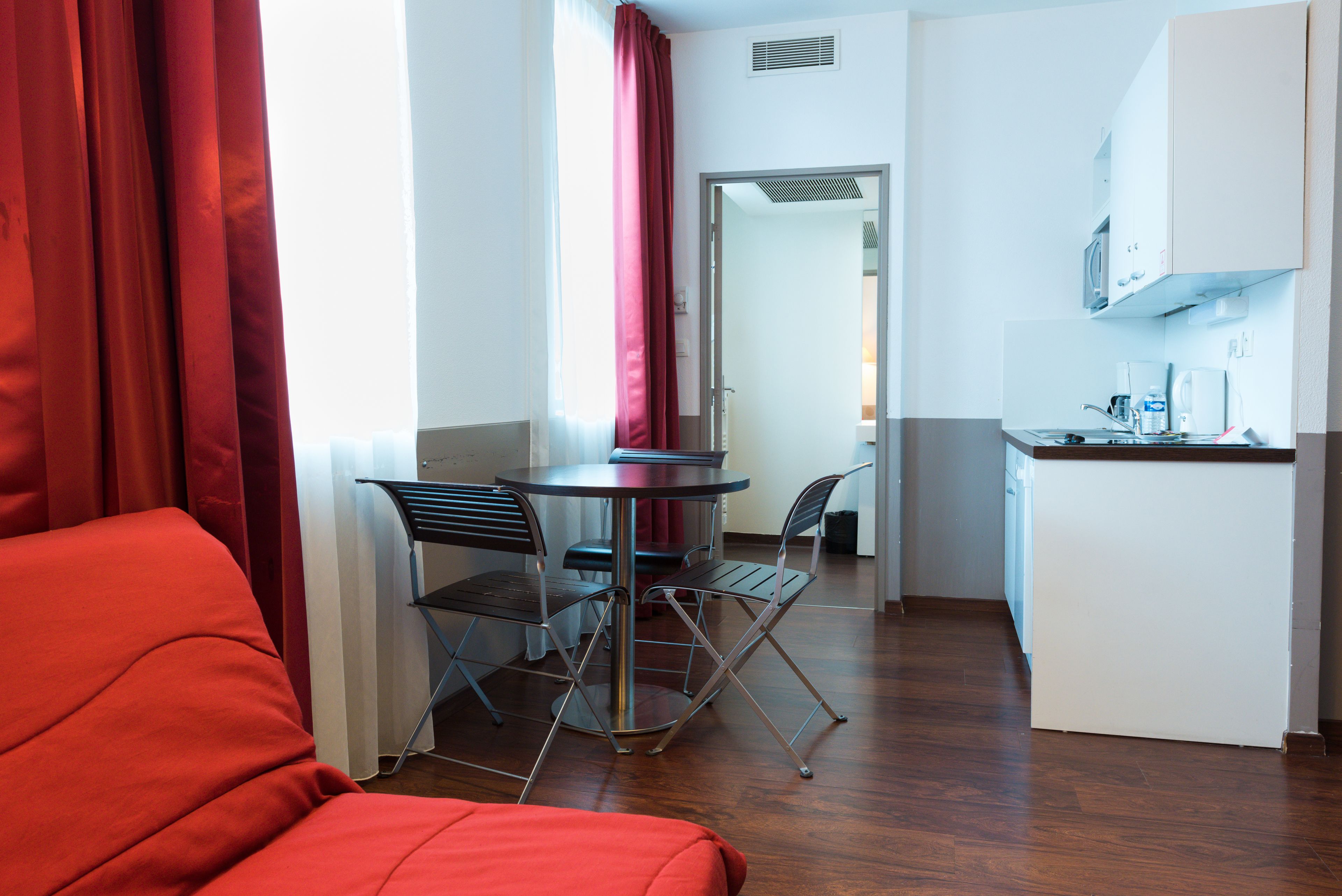 A compact room with a bed, a dining table with chairs, a kitchenette, and a bathroom visible through an open door.