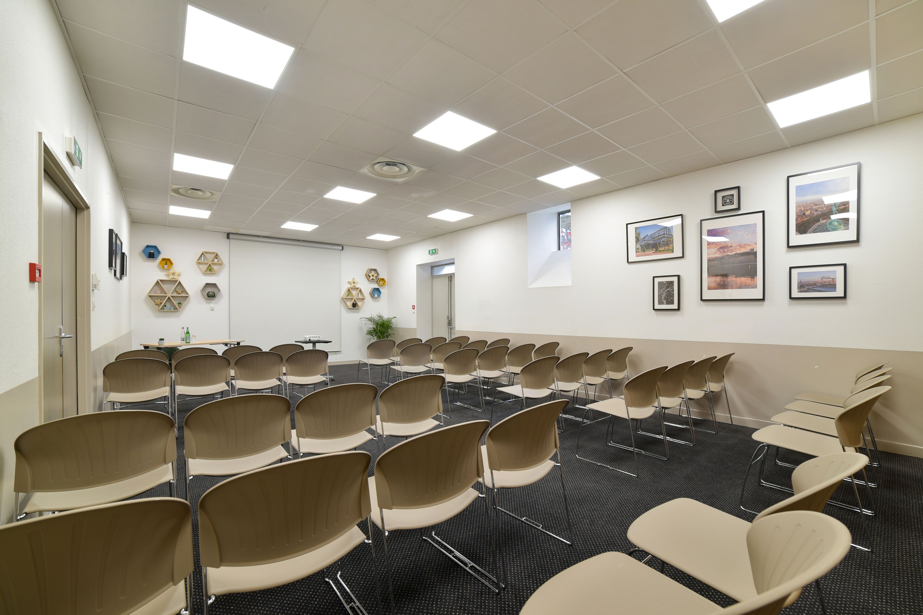 A conference room with rows of chairs, a projector screen, and framed pictures on the walls.