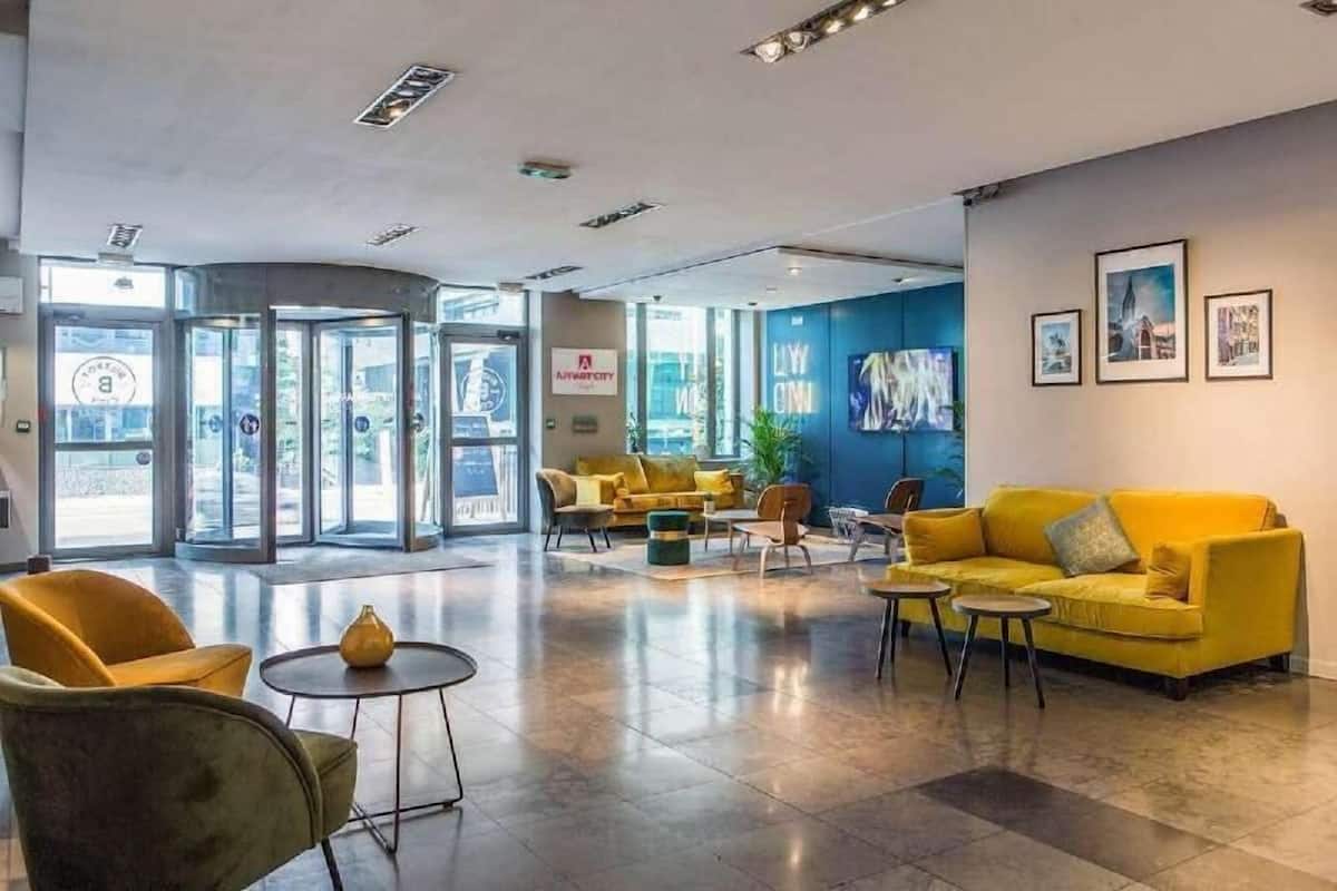 Un lobby moderno con un sofá amarillo, una mesa redonda y una entrada con puerta de vidrio.