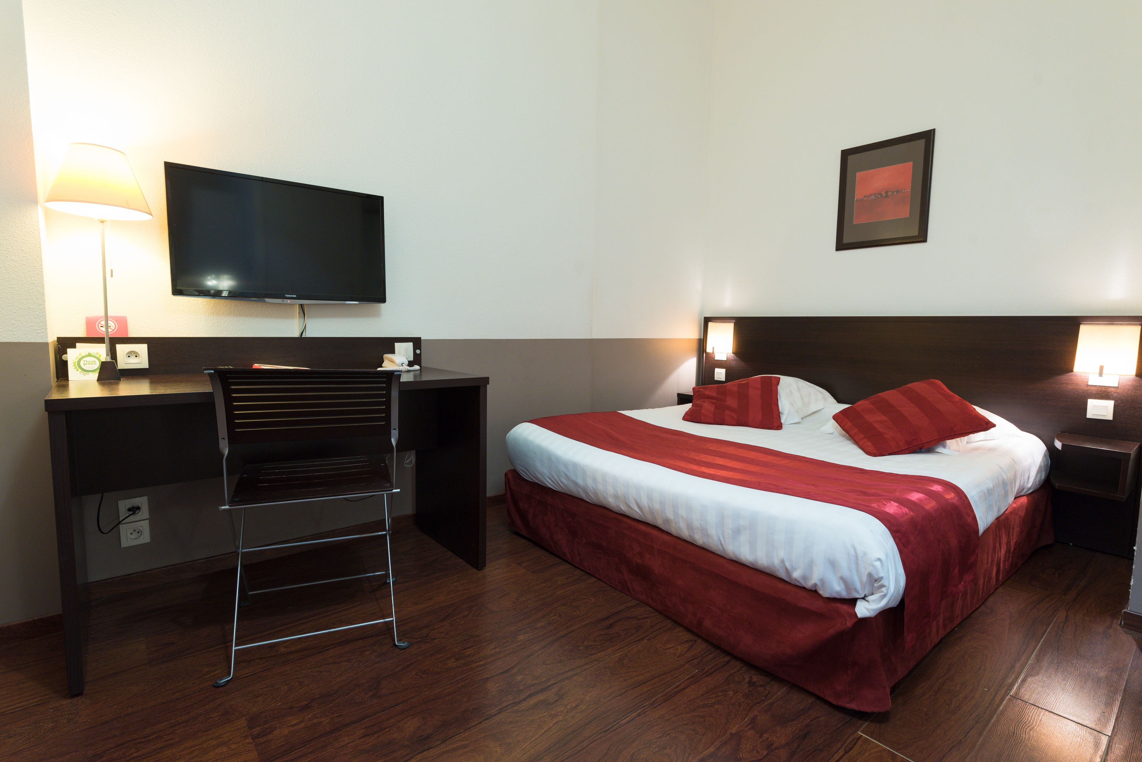 Una habitación de hotel con cama, escritorio, televisor y un cuadro en la pared.
