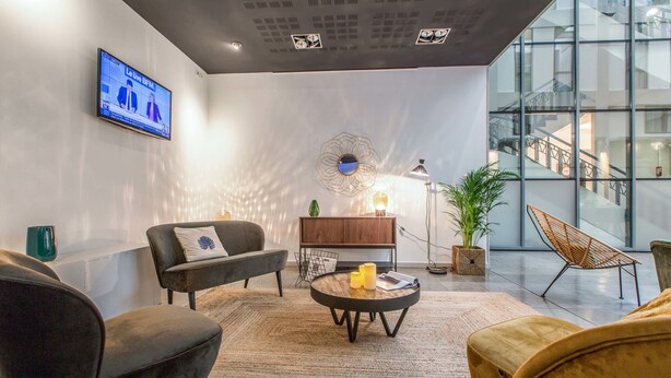 A modern living room with a sofa, armchair, and round coffee table. A television is mounted on the wall, and there is a staircase visible in the background. - Appart'City Classic Lyon Part-Dieu (Lyon)